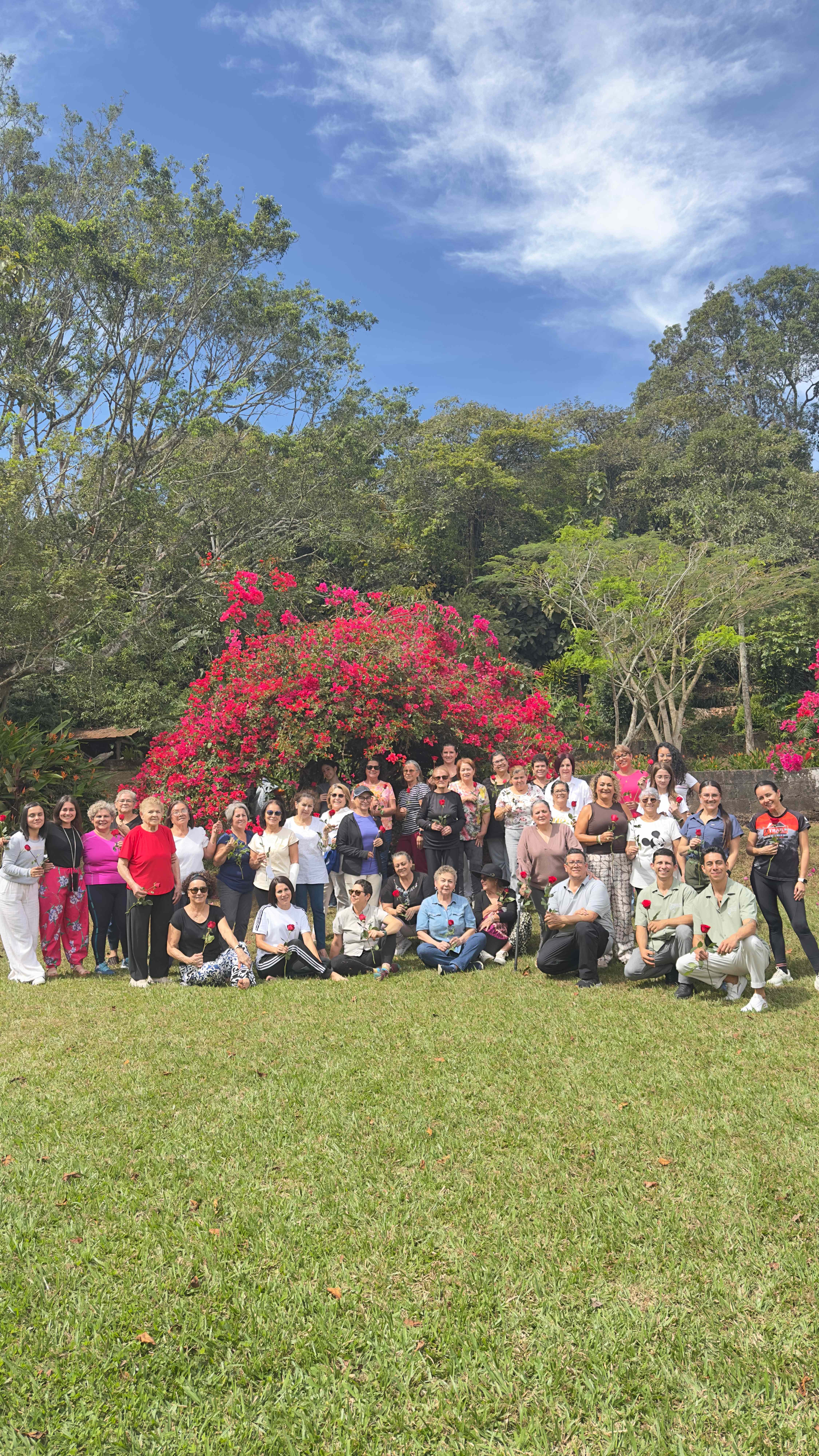 Foto grupal del evento especial con todos los participantes sosteniendo rosas frente a un hermoso arbusto de buganvilias